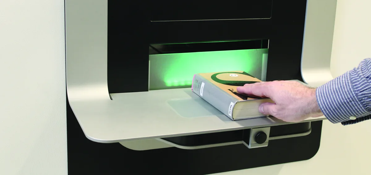 Une main insère un livre dans la fente d'un automate de retour encastré au mur