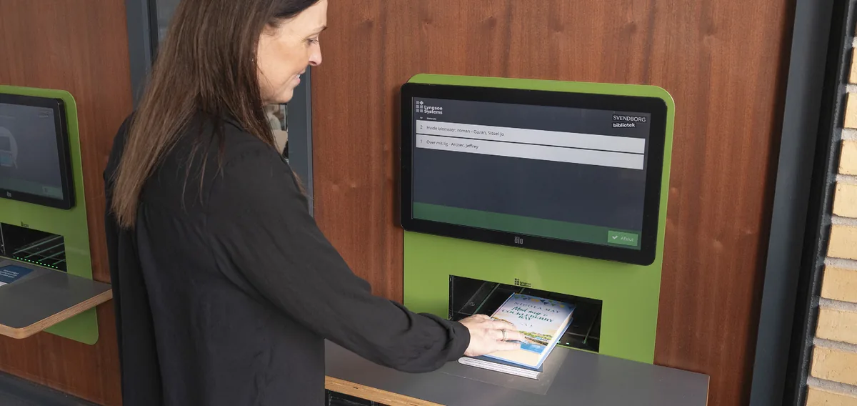 Une bibliothécaire dépose des documents dans un automate de retour encastré dans un habillage bois