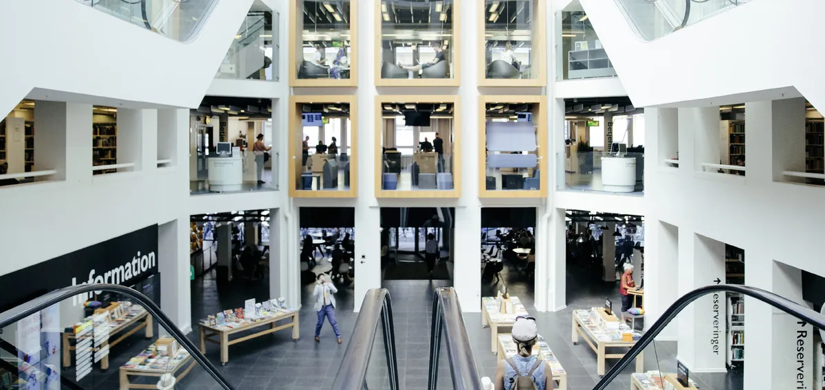 Vue plongeante sur l'atrium d'une grande bibliothèque publique, escaliers mécaniques et tables de présentation