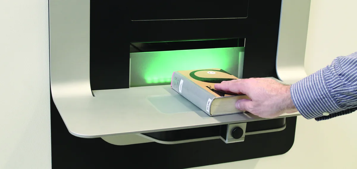 Une main glisse un livre dans la fente éclairée en vert d'un automate de retour