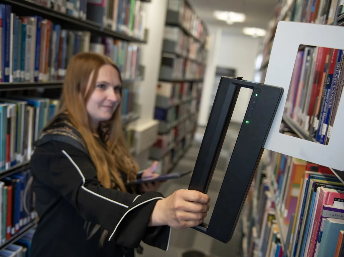 Une bibliothécaire passe un lecteur portable le long d'un rayon
