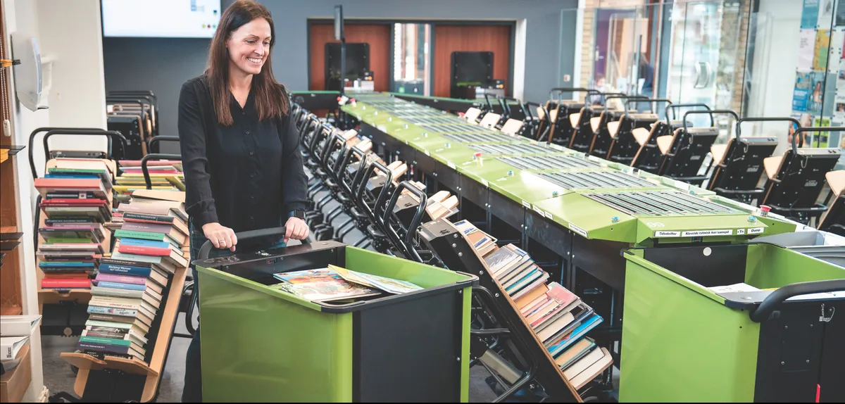 Une bibliothécaire travaille en bout de ligne de tri, les bacs alignés sous les goulottes